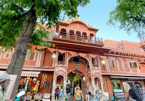 Historic building with intricate architecture, surrounded by greenery and market activity.